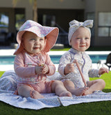 Two babies wearing UV Skinz UPF 50+ swimwear playing sun safe on astroturf by a backyard pool.