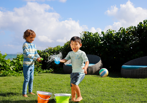 Two boys happily playing together on a Hawaiian beach, both wearing UV Skinz UPF 50+ swimwear and rash guards, well-protected from the sun’s rays as they splash in the water and enjoy outdoor fun.