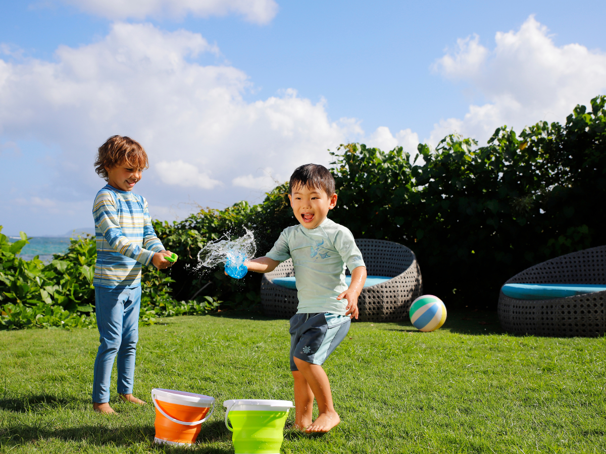 Two boys happily playing together on a Hawaiian beach, both wearing UV Skinz UPF 50+ swimwear and rash guards, well-protected from the sun’s rays as they splash in the water and enjoy outdoor fun.