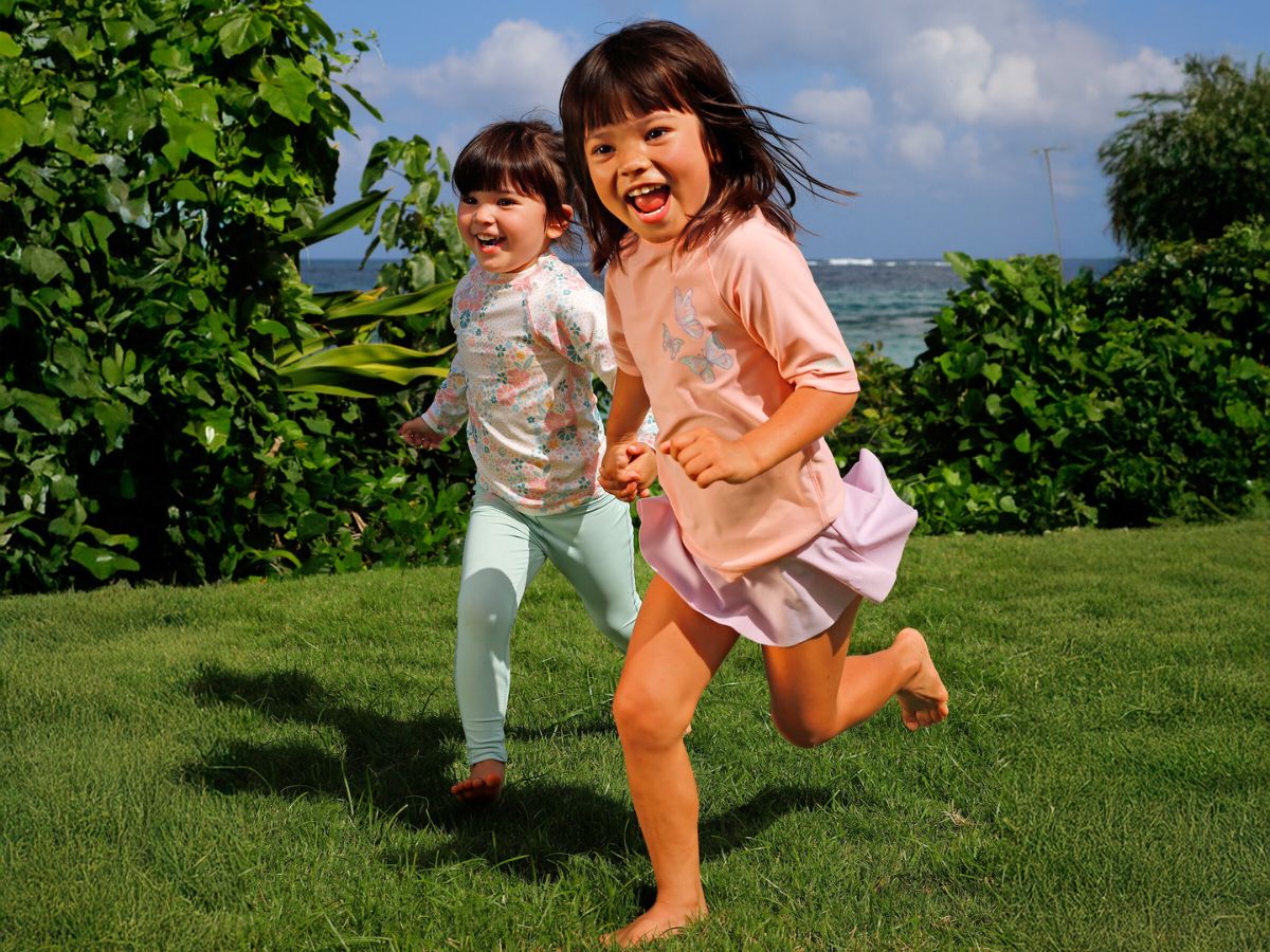 Two young sisters on a sunny spring day, smiling and excited as they participate in a sun-safe backyard scavenger hunt, wearing sun hats and holding a basket to collect their finds.