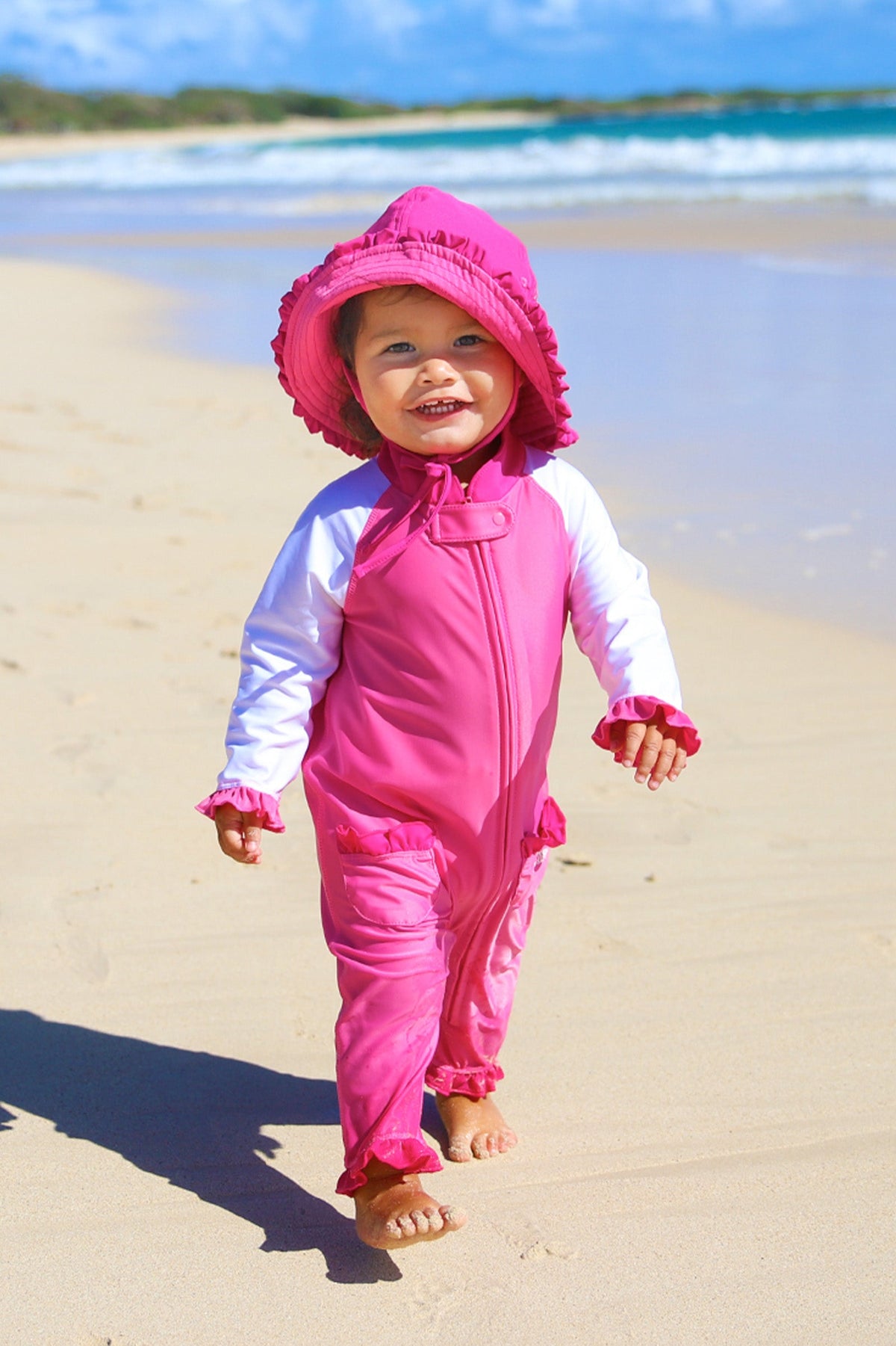Baby girl in UV Skinz's baby girls long-sleeve swimsuit in bubblegum white