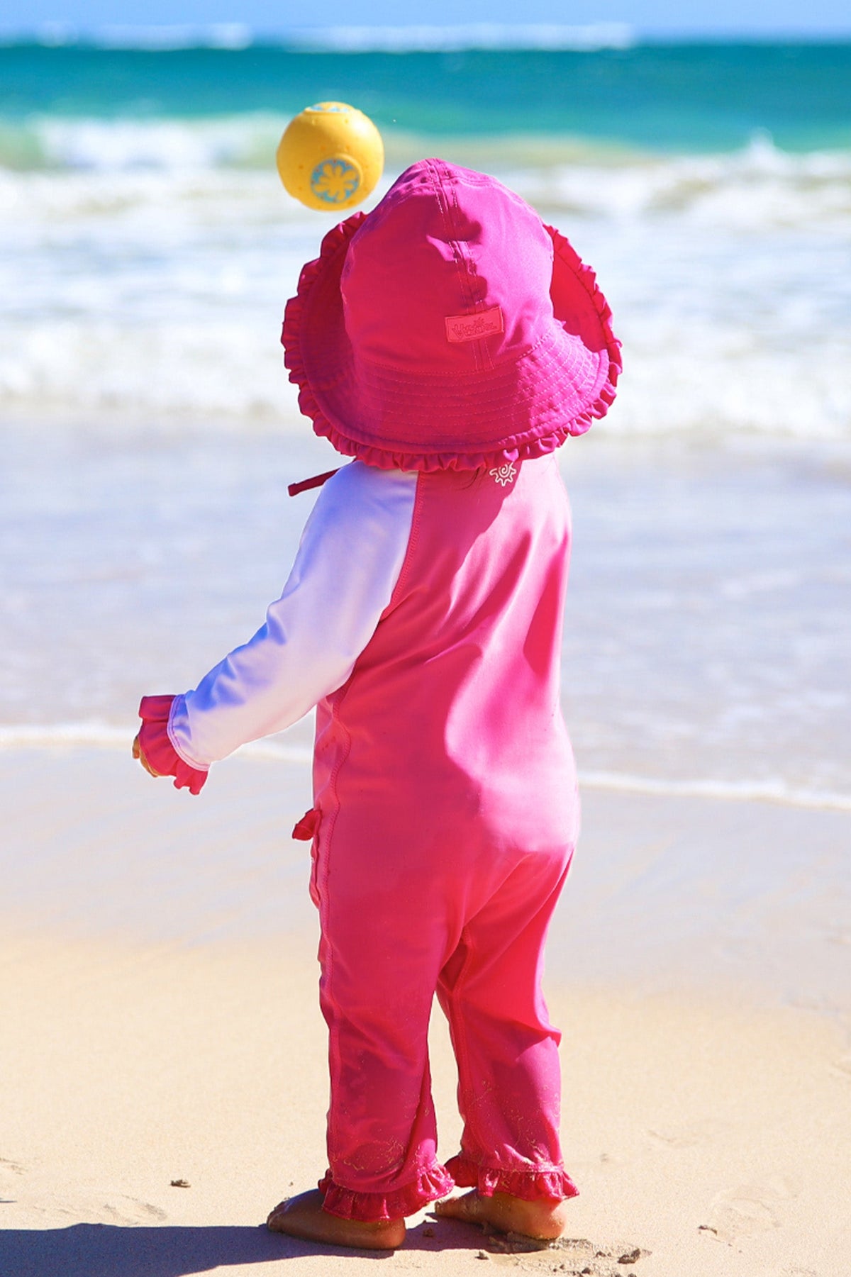 Baby girl in UV Skinz's baby girls long-sleeve swimsuit in bubblegum white on the beach