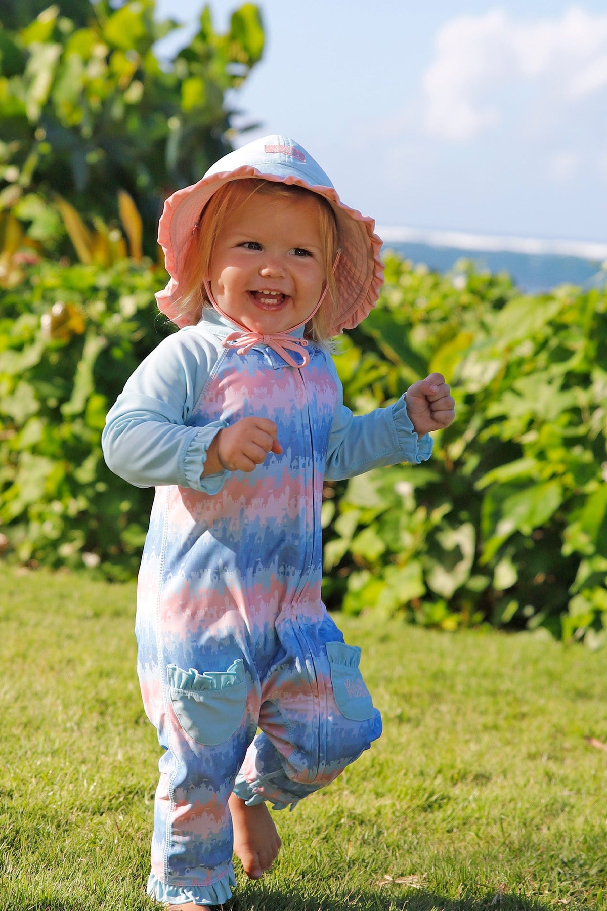 baby girl running in grass in reversible swim hat in aquamarine dusty pink
