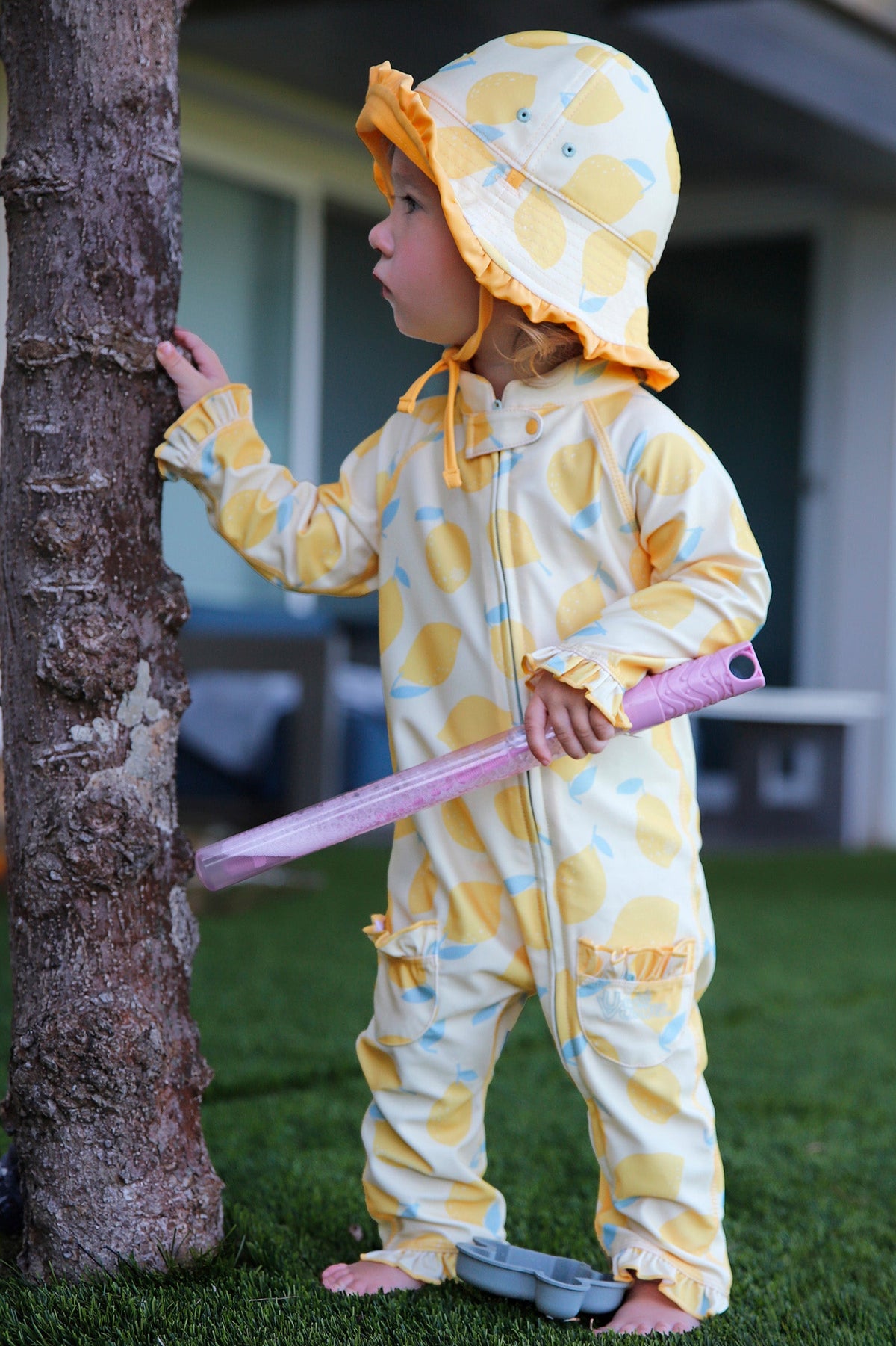 baby girl in grass by tree in baby girl one piece sun & swim suit in lemonade stand
