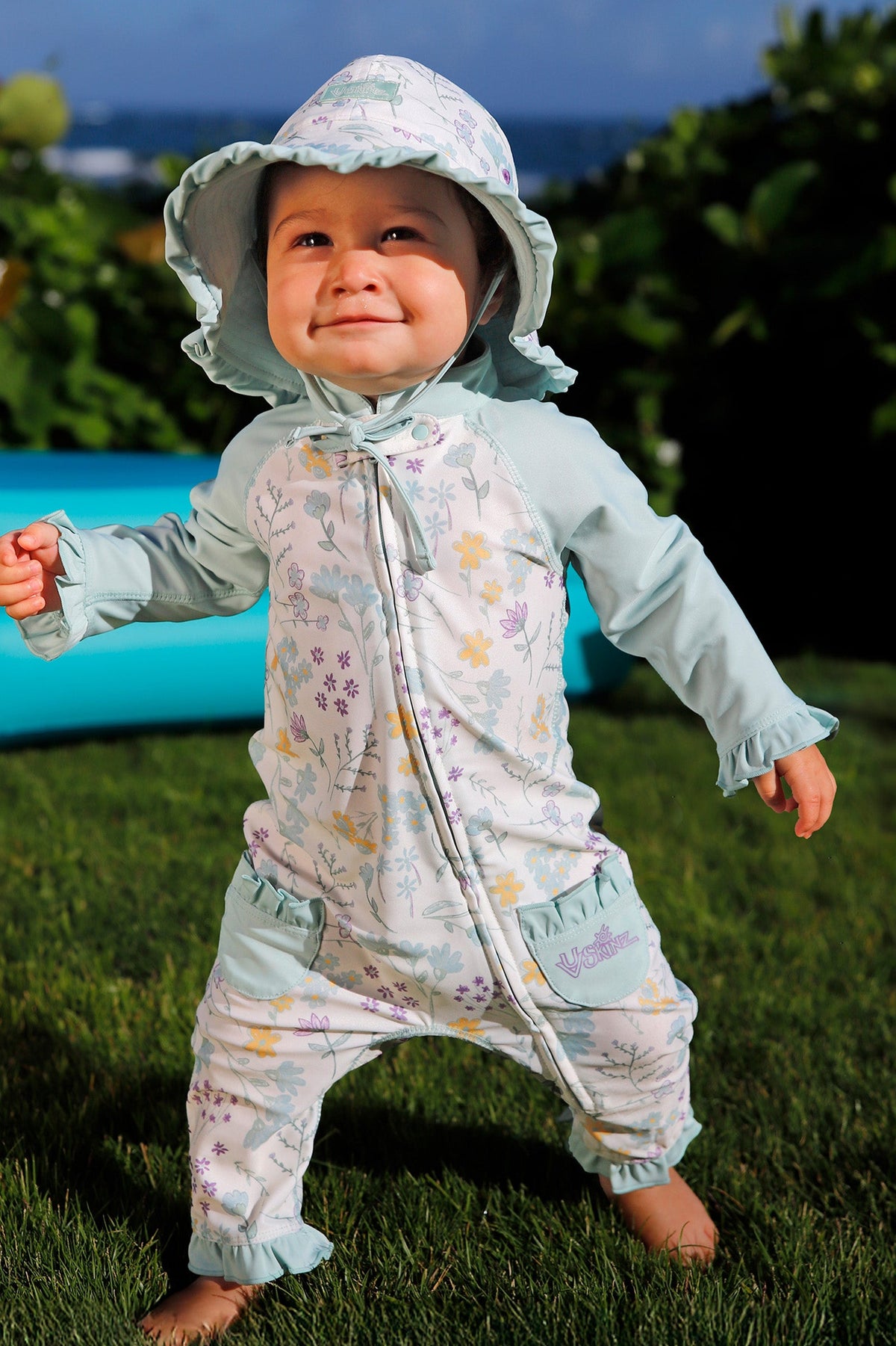 baby girl running in grass in one piece sun & swim suit in springtime doodle