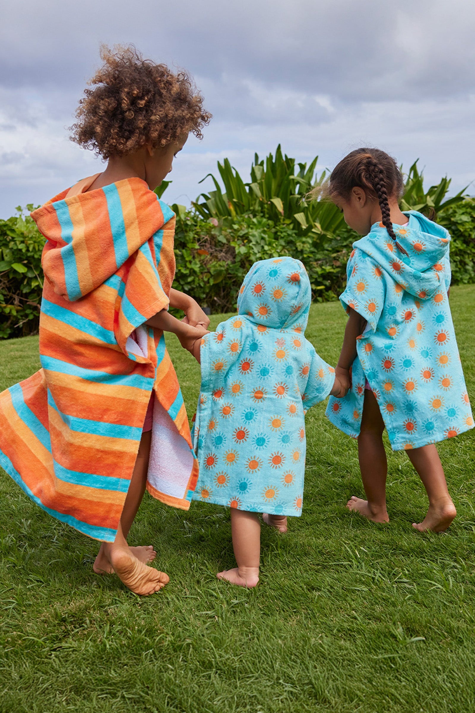 kid's in hooded beach poncho running on grass away|sunny-days