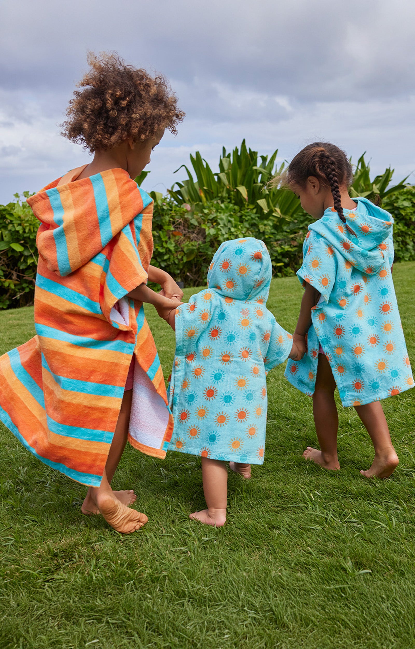 kid's in hooded beach poncho running on grass away|sunny-days
