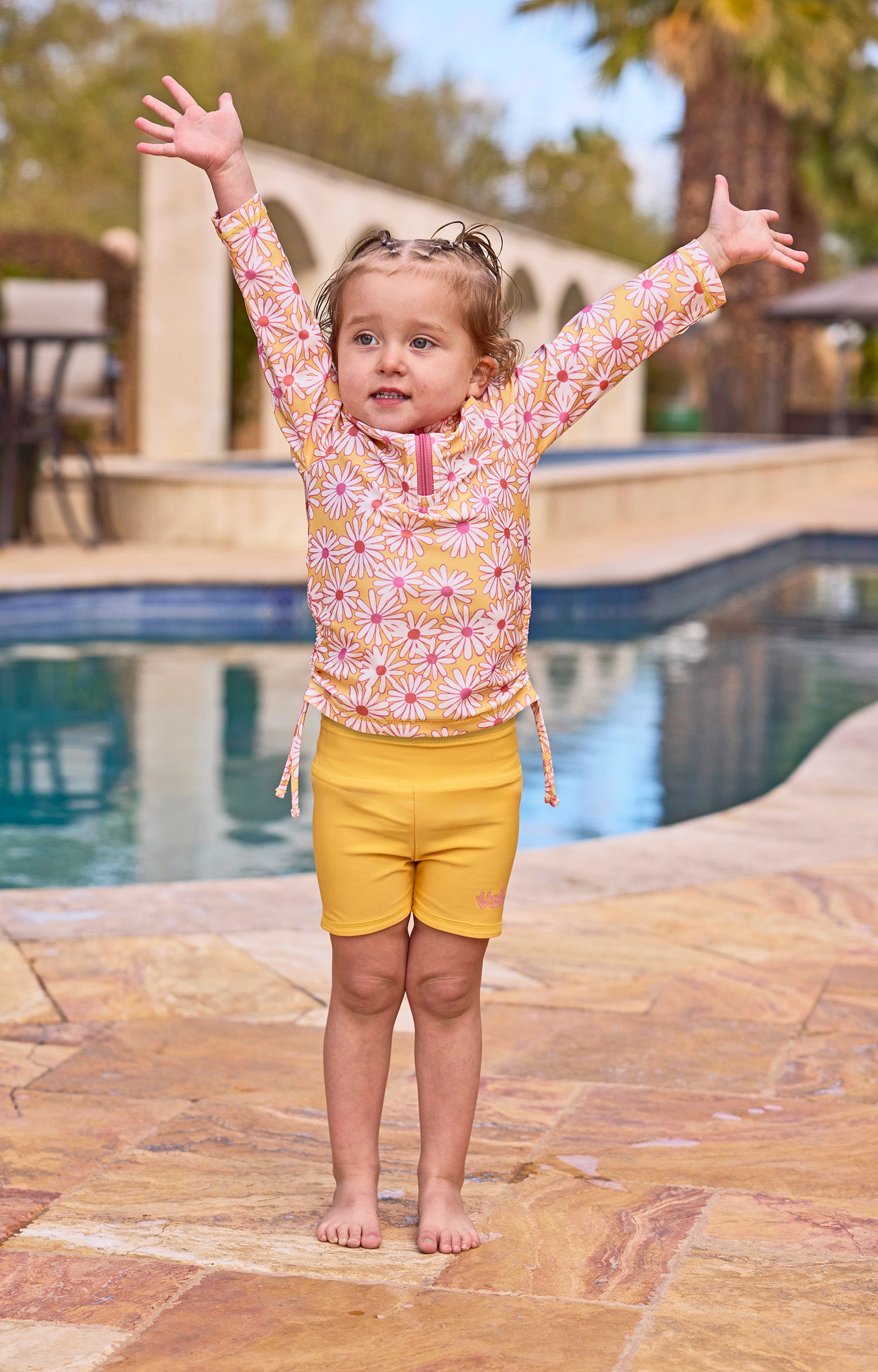 girl with arms up by pool in reversible active swim shorts|sunshine-daisies-marigold