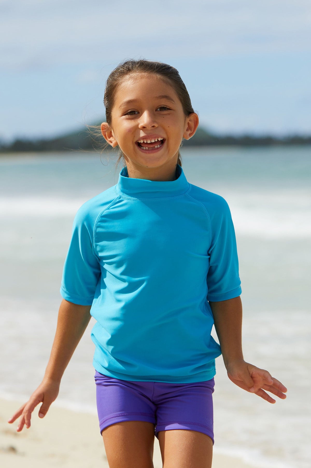 Little girl playing in the ocean in UV Skinz's kid's short sleeve swim shirt in aqua|aqua
