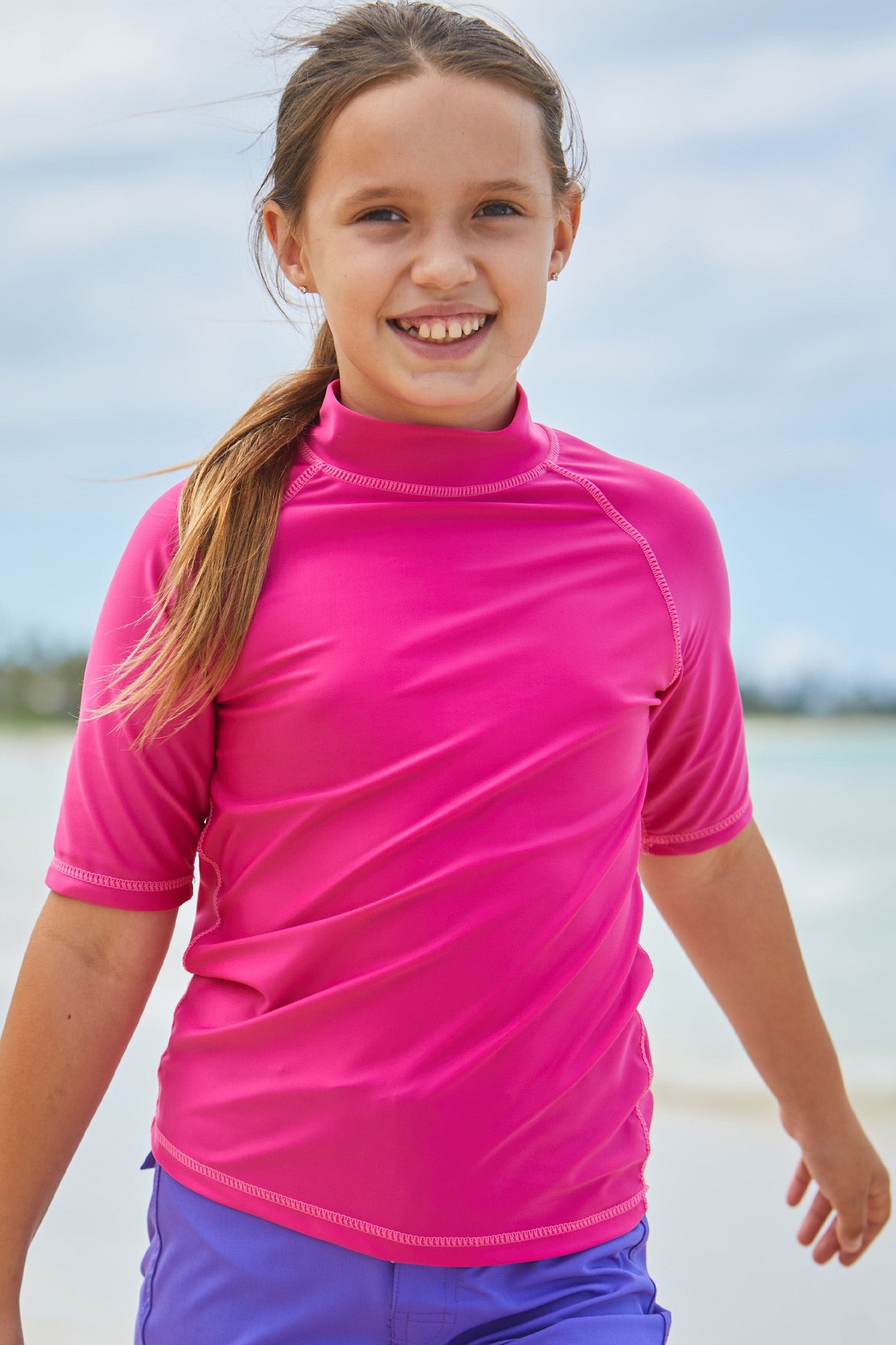 Young girl in UV Skinz's kid's short sleeve swim shirt in hot pink|hot-pink