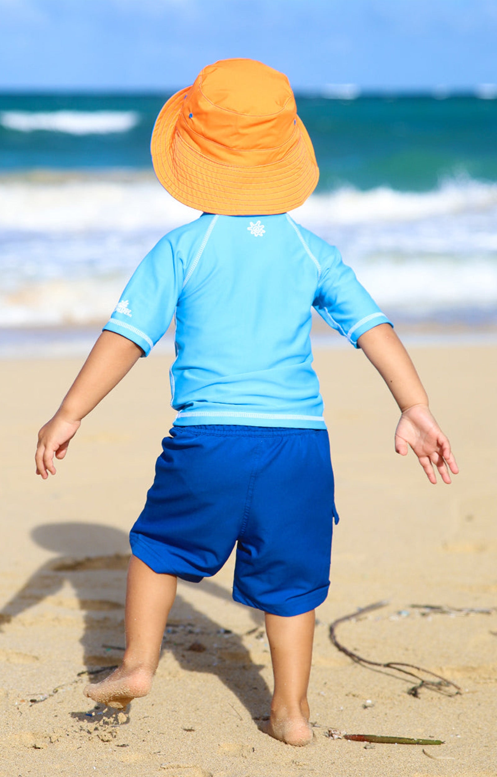 Back of a little boy on the beach in UV Skinz's kid's short sleeve swim shirt|ocean-blue