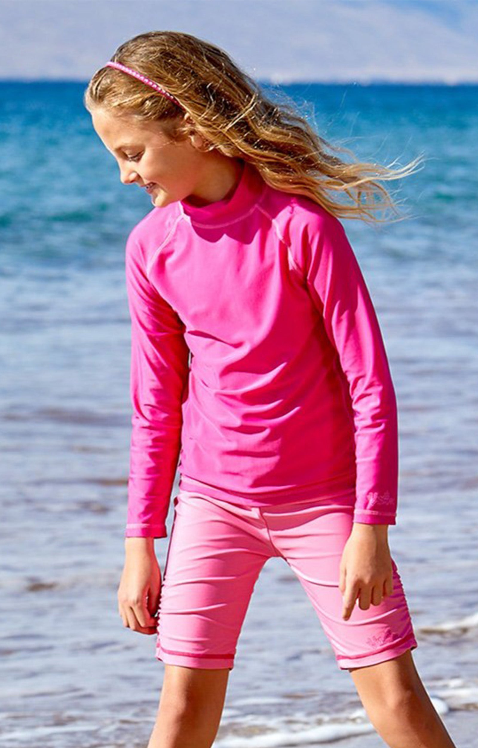 Girl playing in the ocean in UV Skinz's kid's long sleeve swim shirt in hot pink|hot-pink