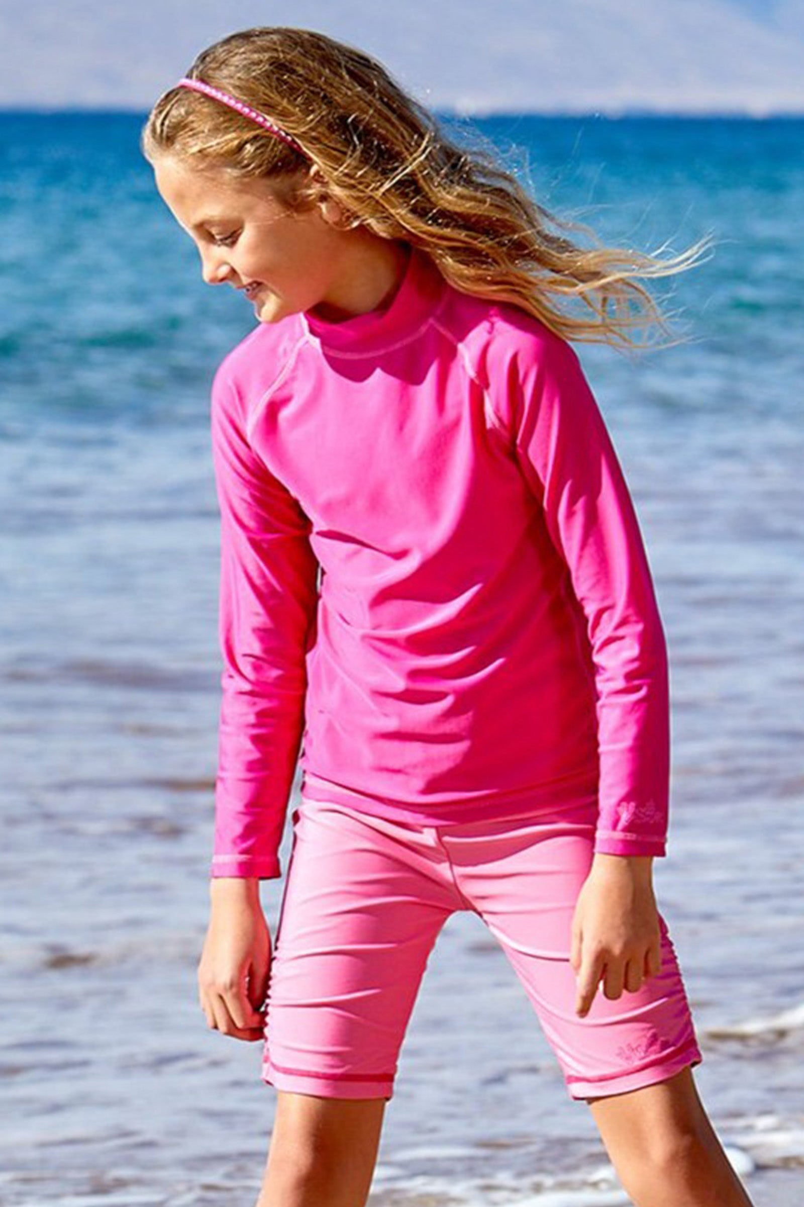 Girl playing in the ocean in UV Skinz's kid's long sleeve swim shirt in hot pink|hot-pink