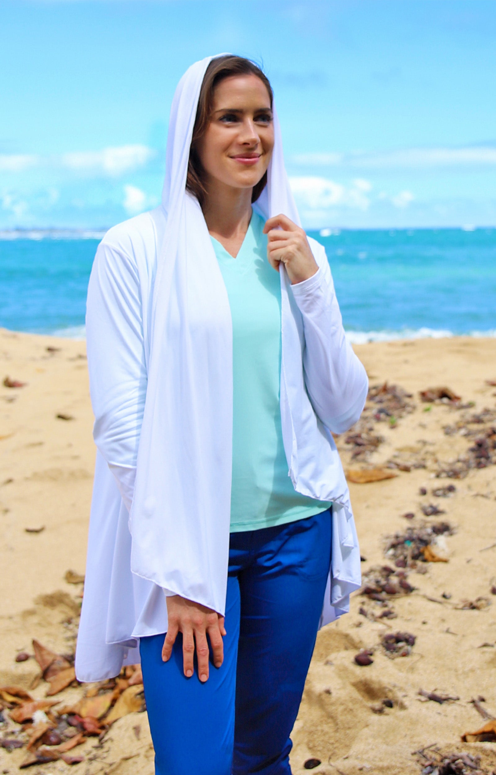 Woman wearing UV Skinz's women's hooded beach cover up in white with the hood on|white