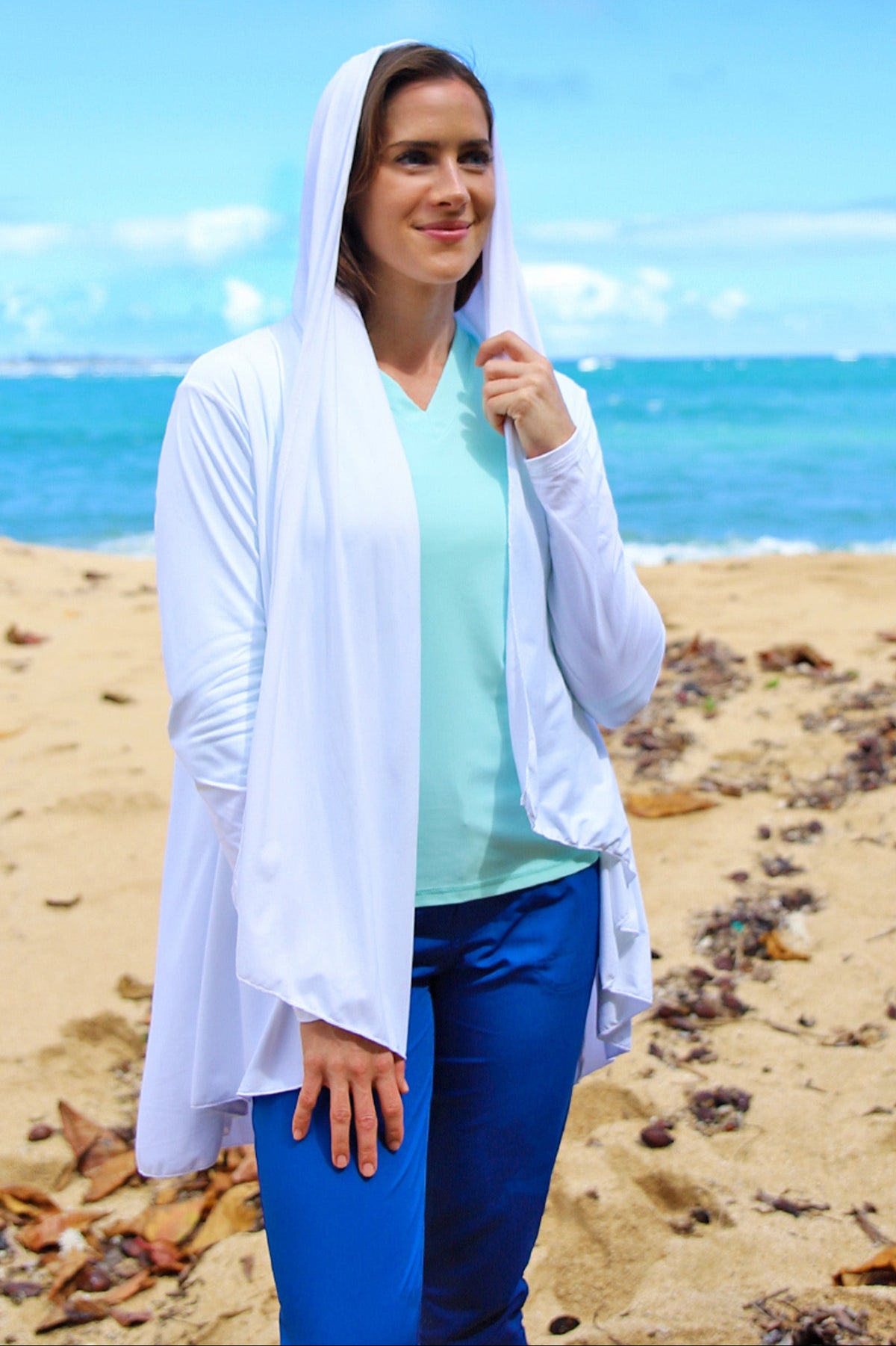 Woman wearing UV Skinz's women's hooded beach cover up in white with the hood on|white