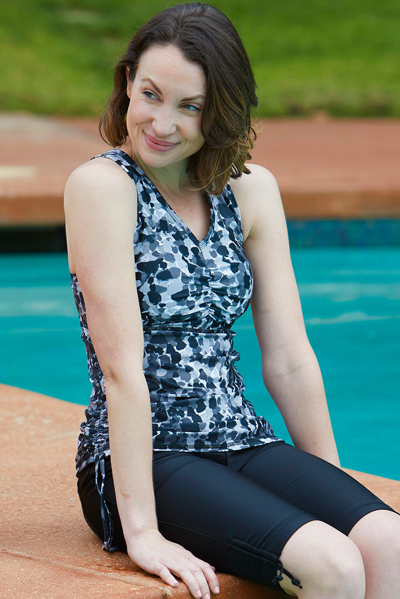 Woman sitting by the pool in the women's ruched swim tank top in black sea glass|black-sea-glass