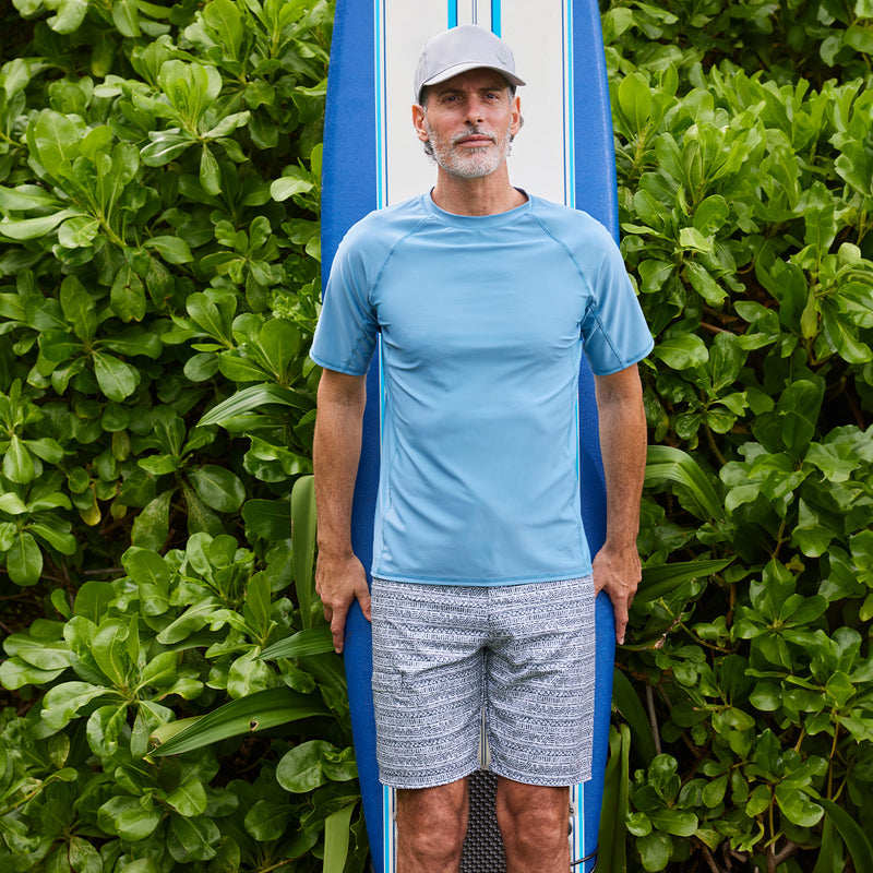 man in front of surfboard in men's coastal board shorts|cool-grey-aztec-stripe