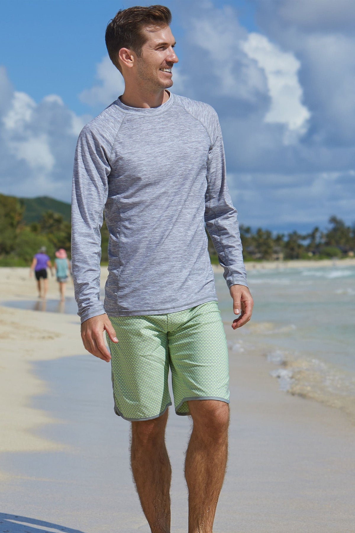 Man on the beach in UV Skinz's men's board shorts in electric green zigzag|electric-green-zigzag