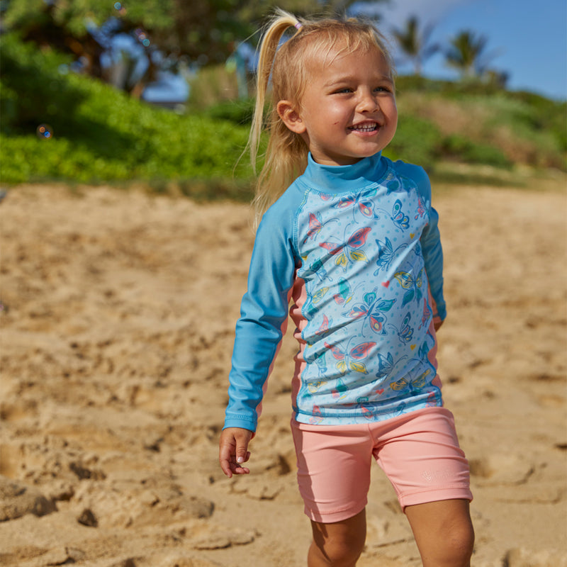 Baby girl on the beach in UV Skinz's girl's swim shorts in apricot|apricot