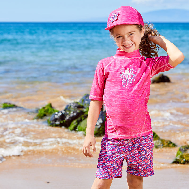 Girl on the beach in UV Skinz's girl's short sleeve sport sun and swim shirt in jaspe hot pink octopus|jaspe-hot-pink-octopus