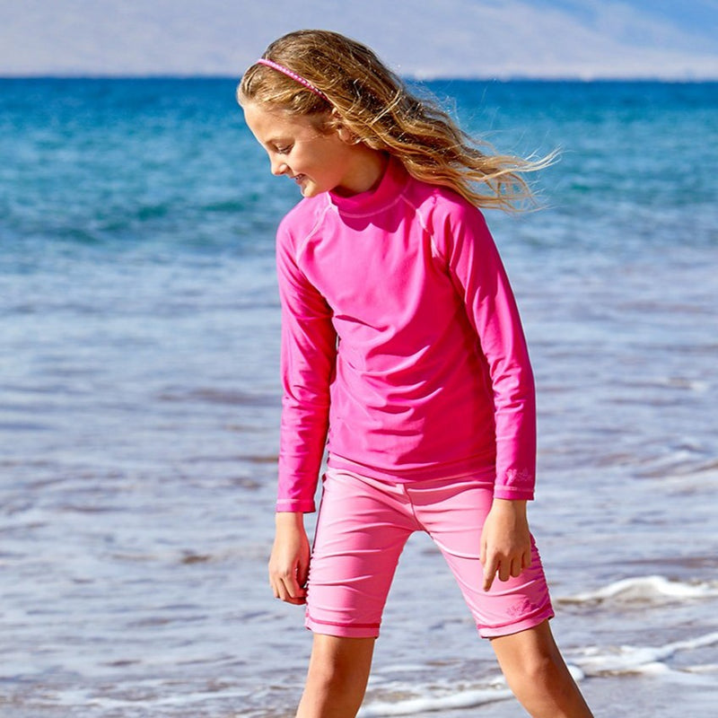 Girl playing in the ocean in UV Skinz's kid's long sleeve swim shirt in hot pink|hot-pink