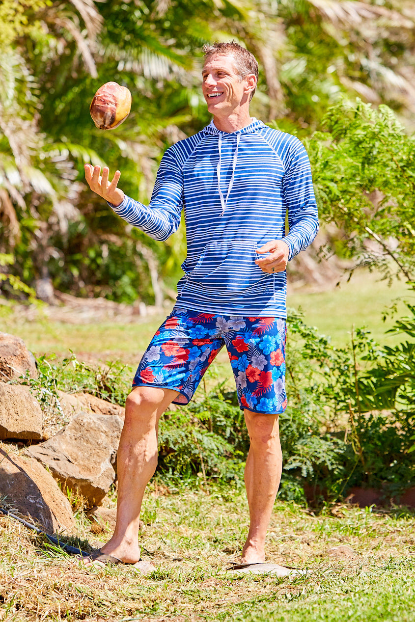Man tossing a coconut on the beach in UV Skinz's men's retro board shorts in americana hibiscus|americana-hibiscus