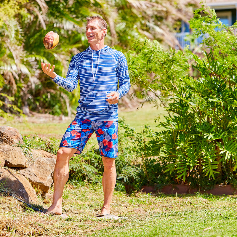 Man tossing a coconut on the beach in UV Skinz's men's retro board shorts in americana hibiscus|americana-hibiscus