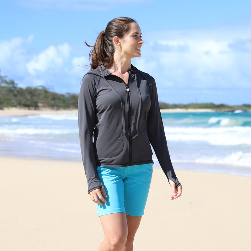 Woman on the beach in UV Skinz's UV Skinz's women's hooded water jacket in charcoal|charcoal