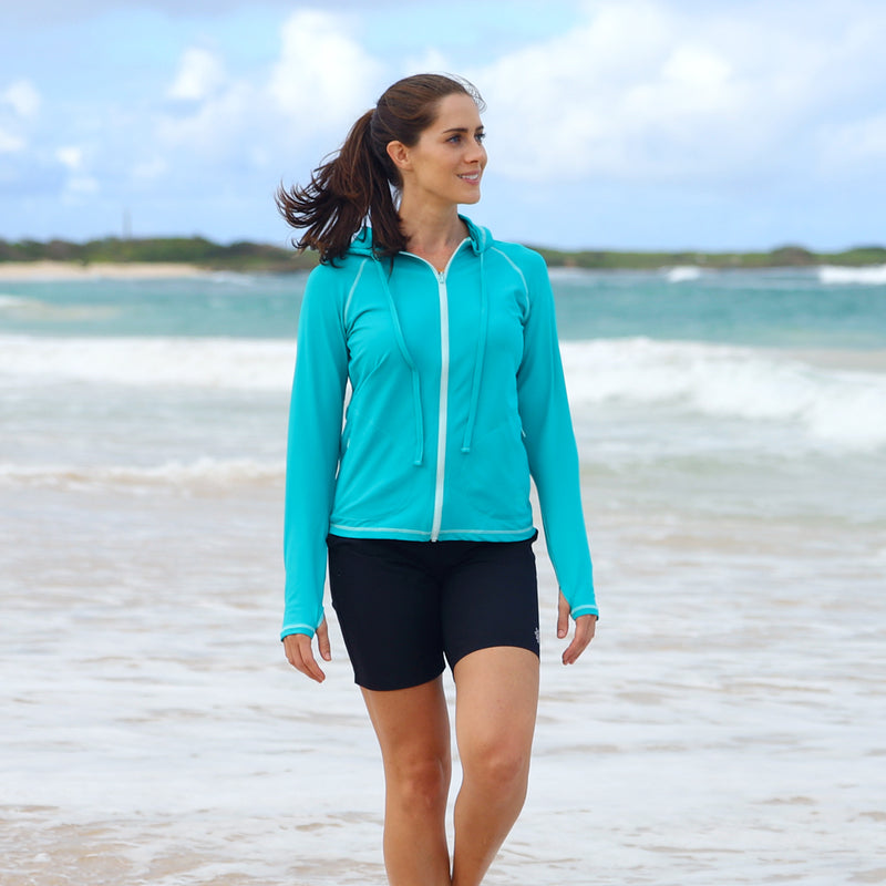Woman wearing the UV Skinz's women's hooded water jacket in teal on the beach|teal