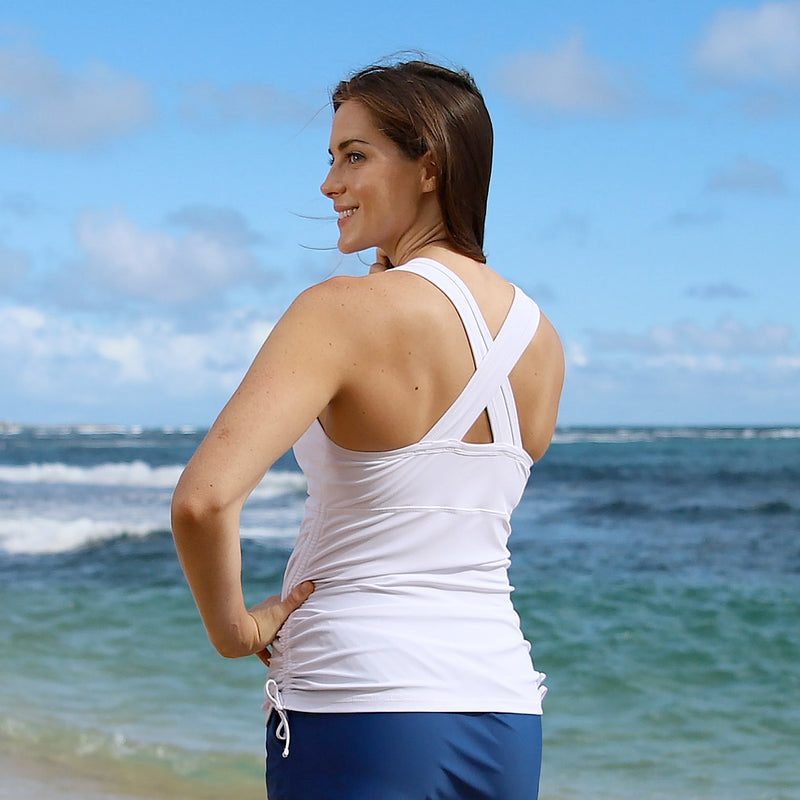 Back of a woman posing on the beach in UV Skinz's women's ruched swim tank top in white|white