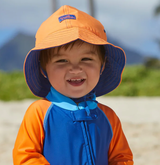 A young baby boy in a sun hat on his first day at the beach