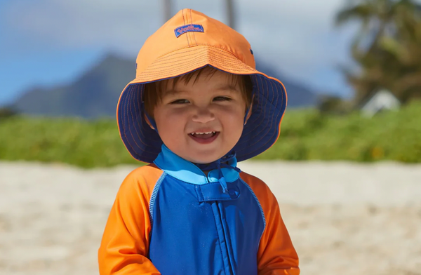 A young baby boy in a sun hat on his first day at the beach