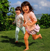 Two young sisters on a sunny spring day, smiling and excited as they participate in a sun-safe backyard scavenger hunt, wearing sun hats and holding a basket to collect their finds.