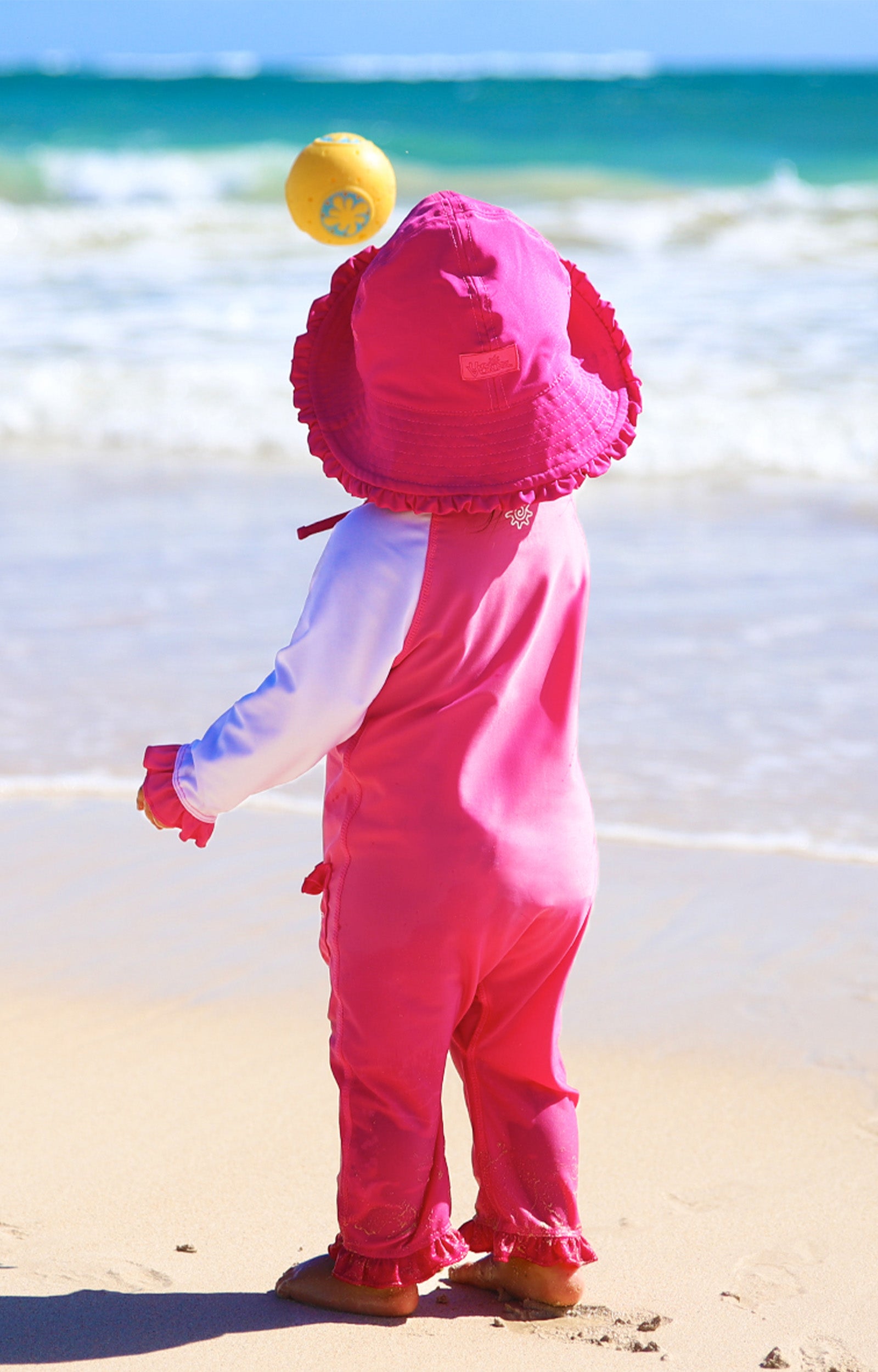 Baby girl in UV Skinz's baby girls long-sleeve swimsuit in bubblegum white on the beach|bubblegum-white
