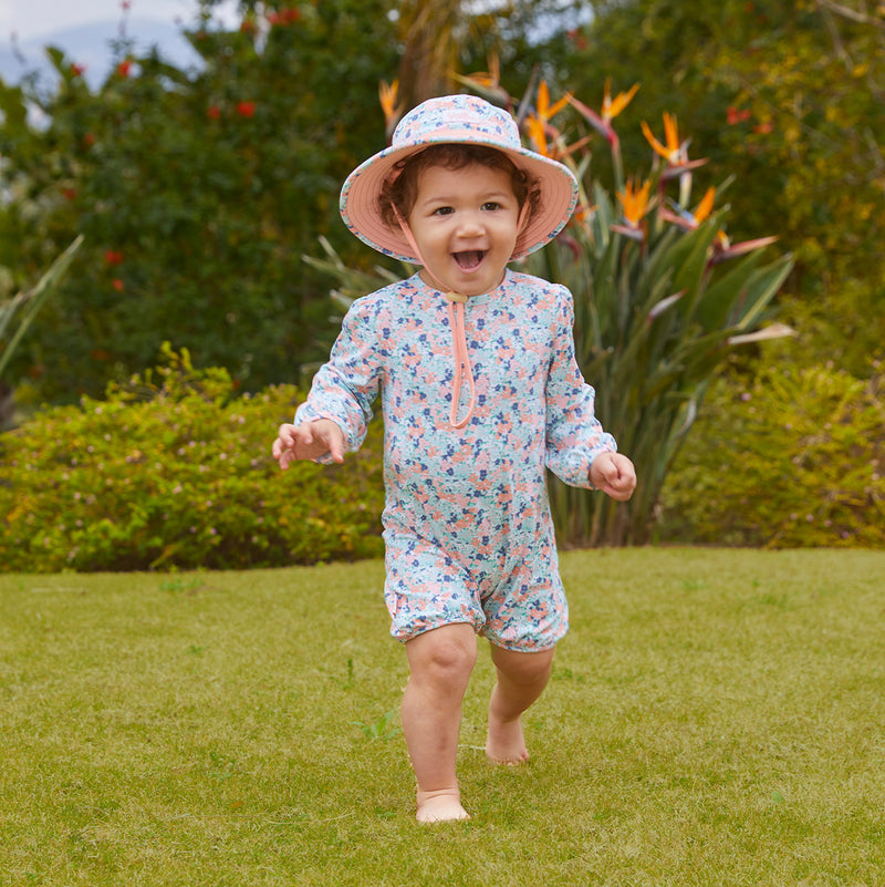 Baby girl playing in UV Skinz's baby girl's one-piece swimsuit in meadow bloom|meadow-bloom