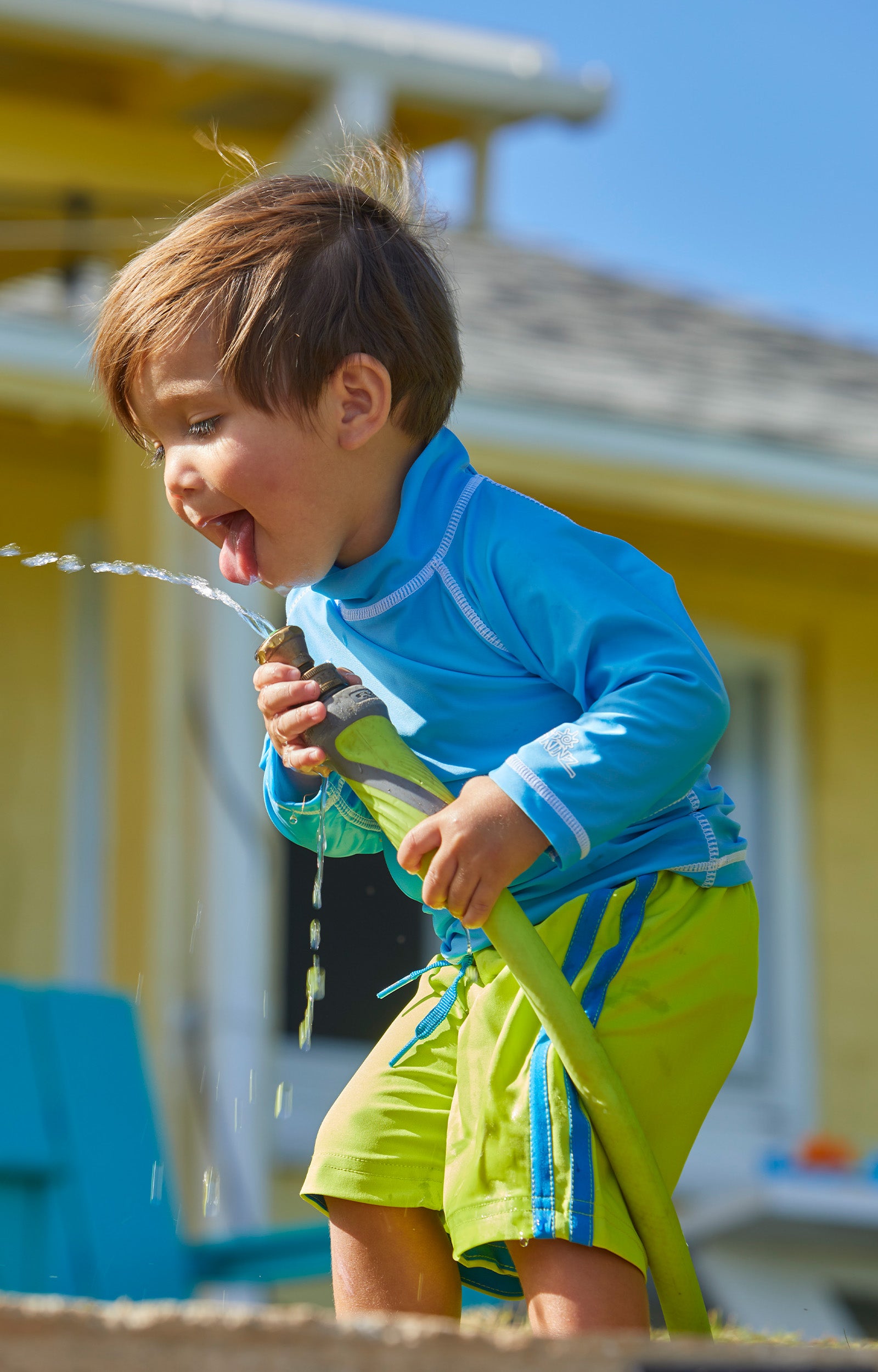 Baby boy playing with a hose in UV Skinz's baby long sleeve swim shirt in ocean blue|ocean-blue
