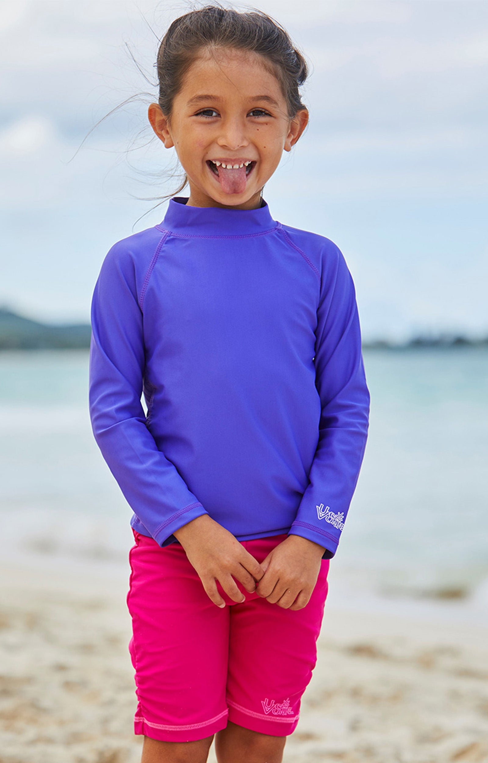 Little girl on the beach in UV Skinz's hot pink swim shorts|hot-pink
