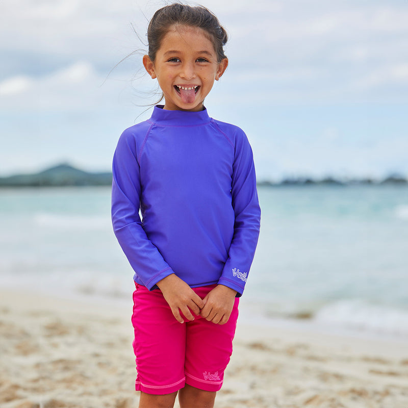 Little girl on the beach in UV Skinz's hot pink swim shorts|hot-pink