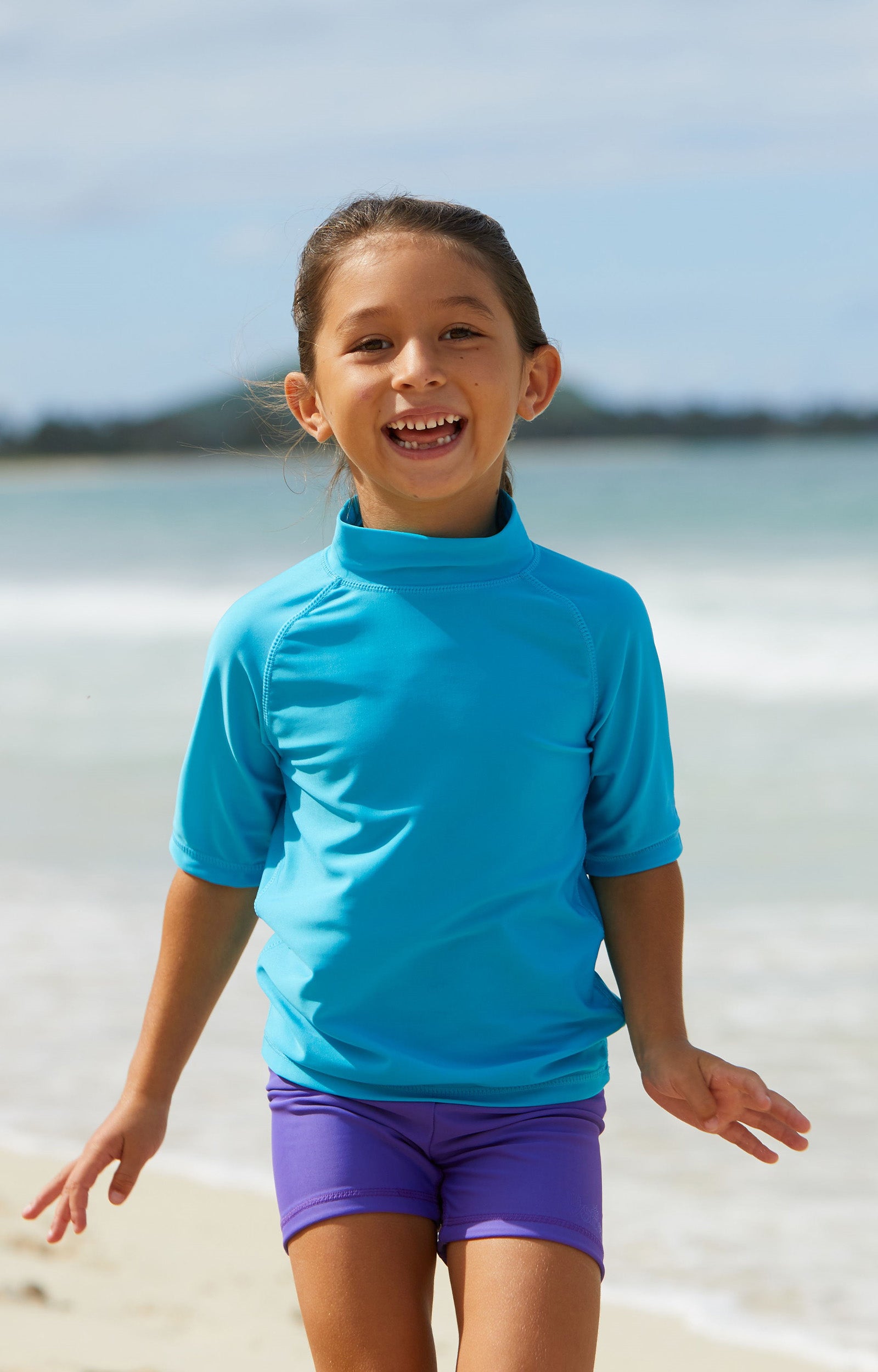Little girl playing in the ocean in UV Skinz's kid's short sleeve swim shirt in aqua|aqua