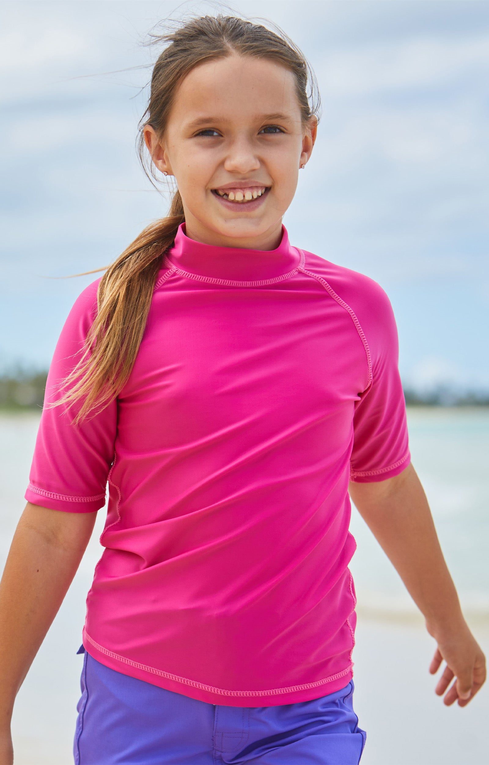 Young girl in UV Skinz's kid's short sleeve swim shirt in hot pink|hot-pink