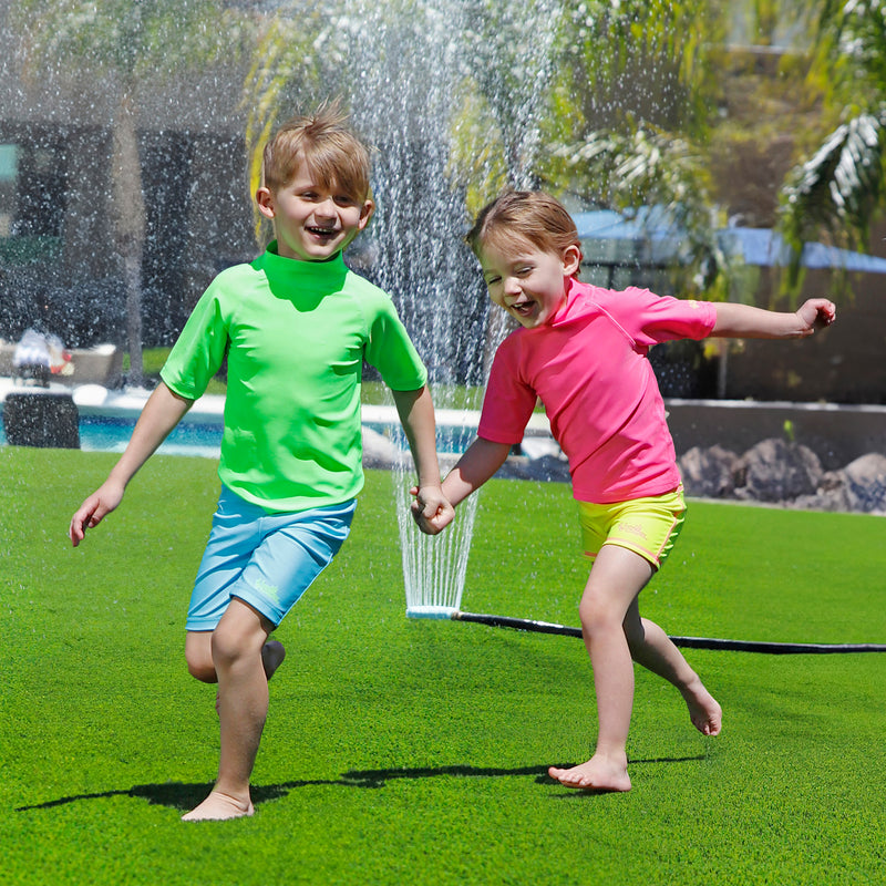 boy having fun in the sprinklers wearing kids neon swim and play jammerz|neon-green