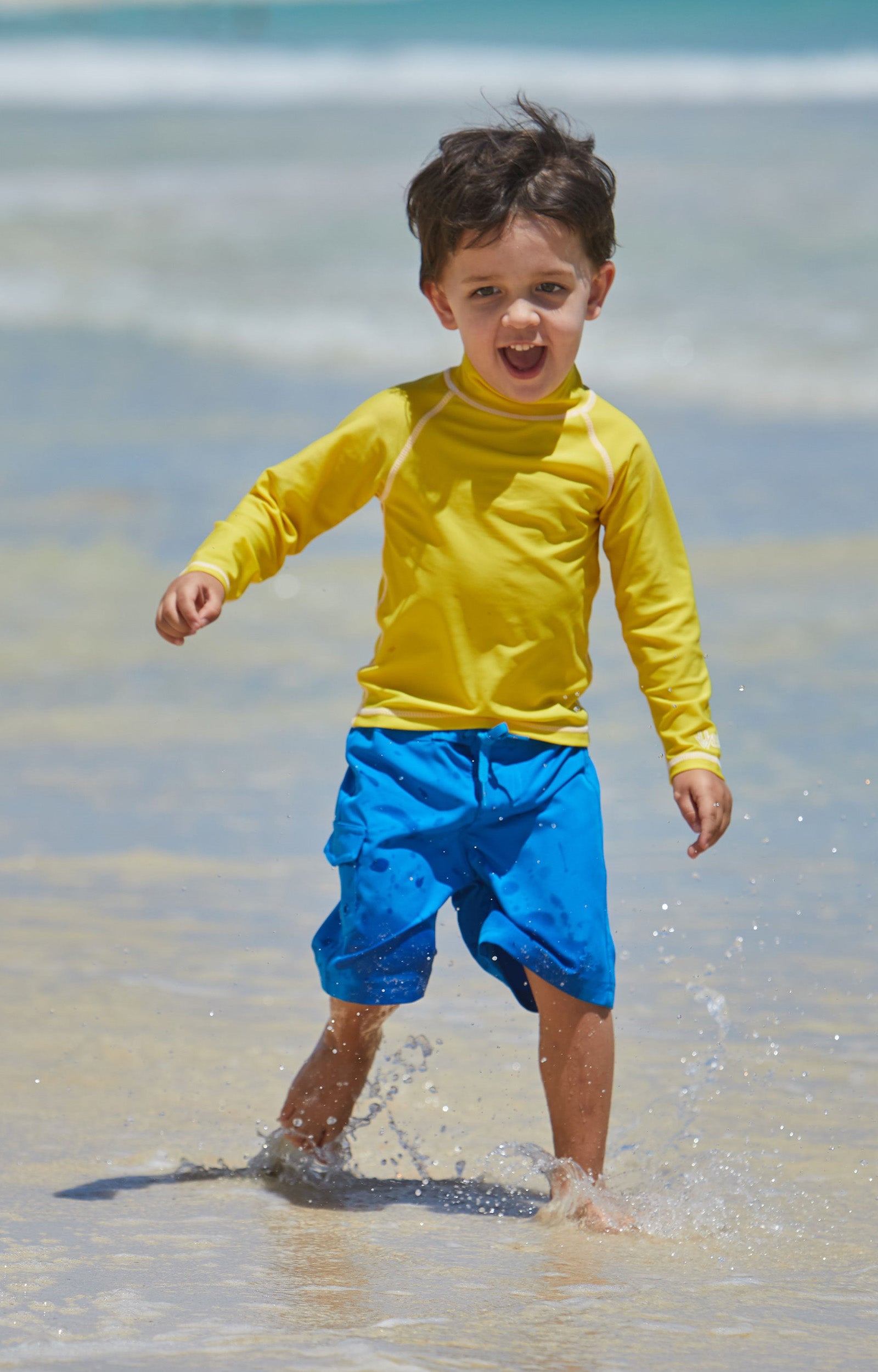 Little boy playing in the ocean in the kid's long sleeve swim shirt in cyber yellow|cyber-yellow