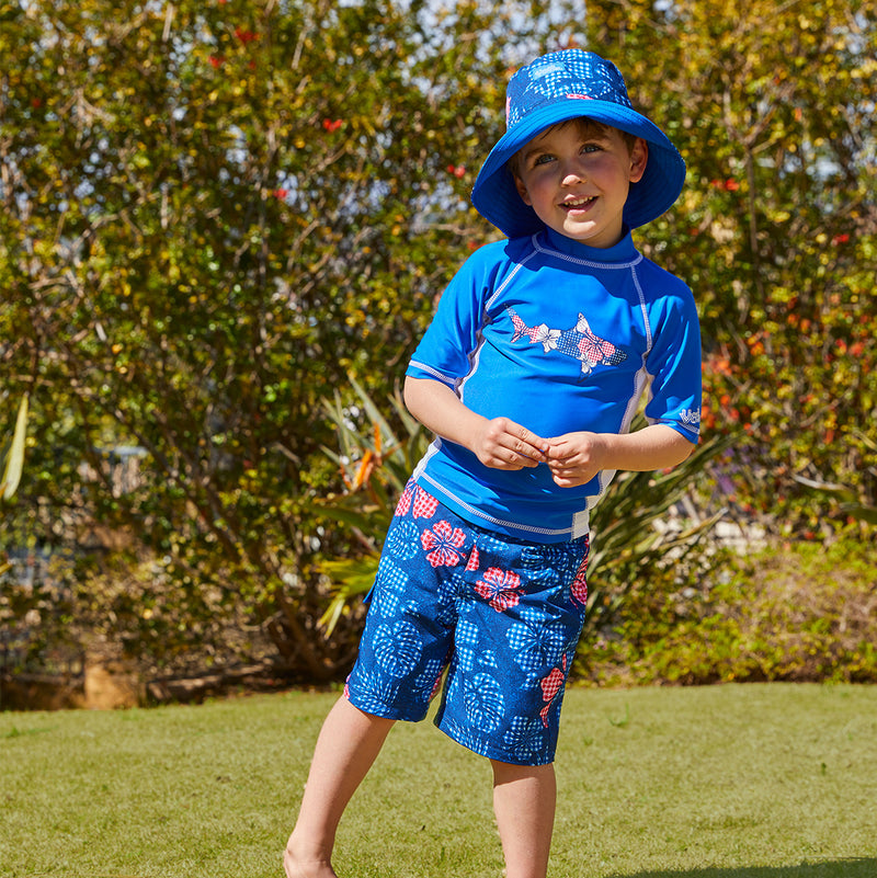 Little Boy in UV Skinz's Boy's Classic Board Shorts in Dark Navy Hibiscus|dark-navy-hibiscus