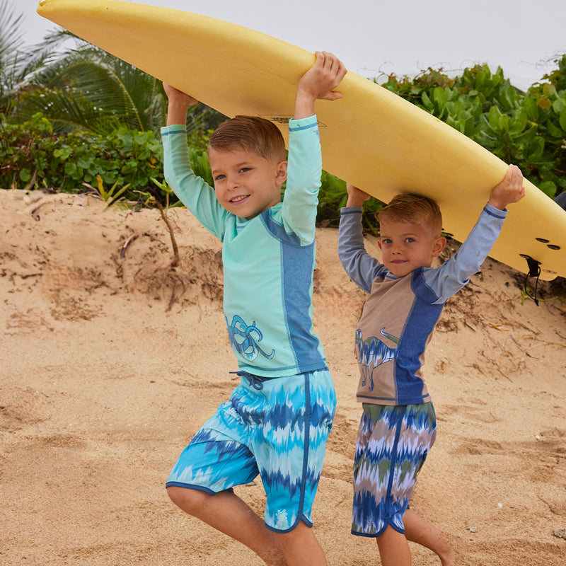 boys on beach carrying surfboards in retro board shorts|aruba-ombre