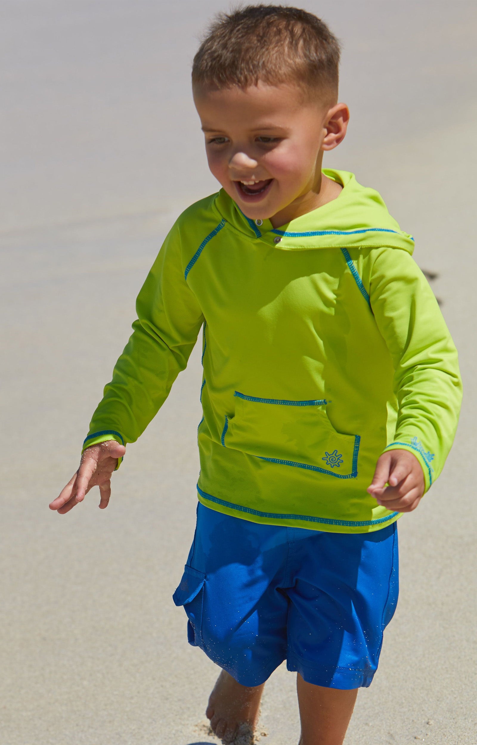 Little boy playing on the beach in UV Skinz's boy's pullover hoodie in lime punch|lime-punch