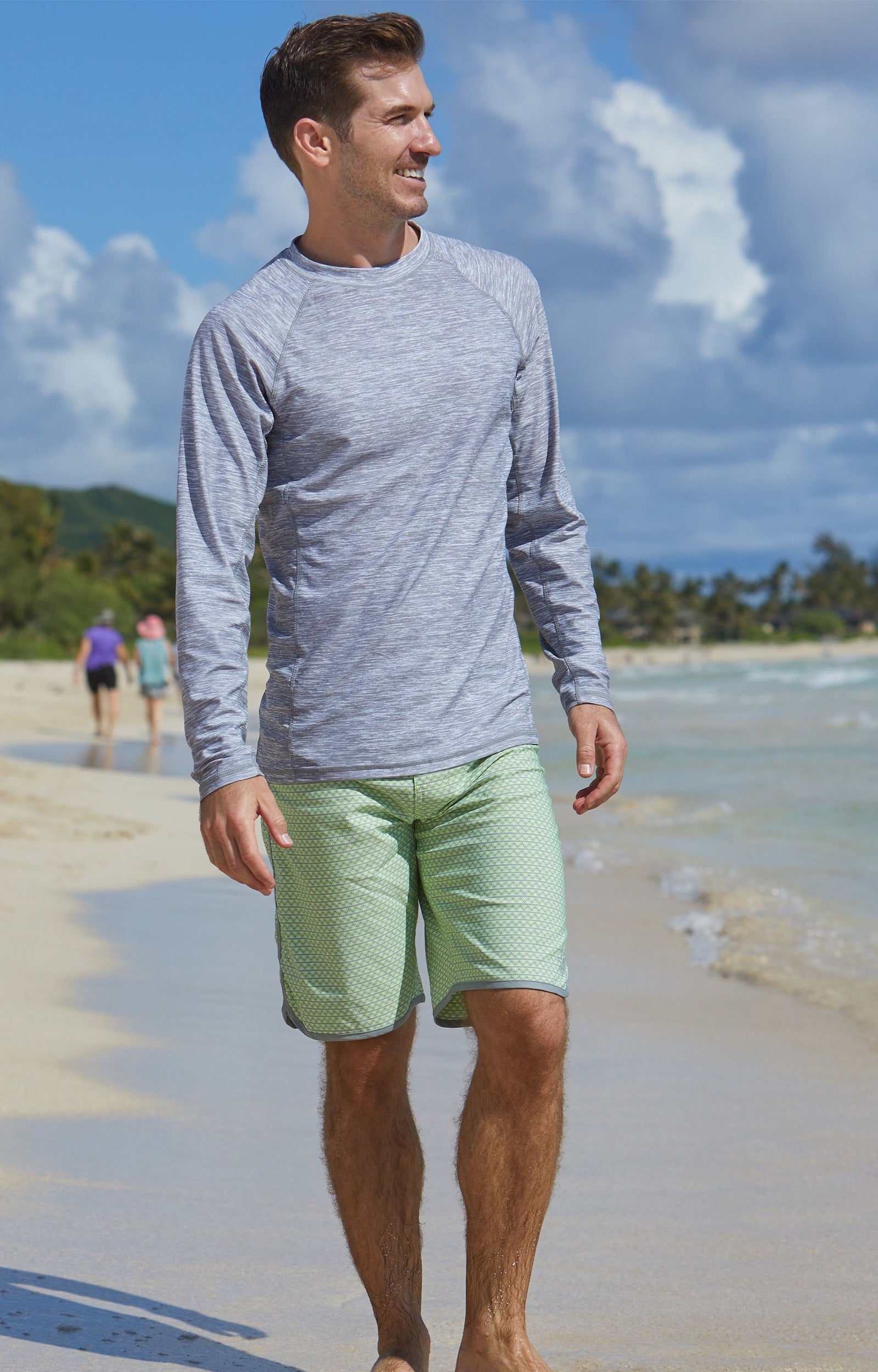 Man on the beach in UV Skinz's men's board shorts in electric green zigzag|electric-green-zigzag