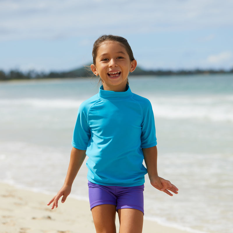 Little girl playing in the ocean in UV Skinz's kid's short sleeve swim shirt in aqua|aqua