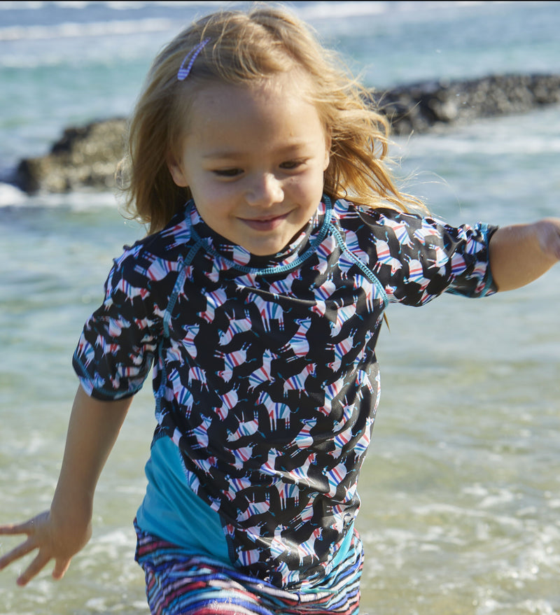 Little girl in UV Skinz's girl's short sleeve sport sun and swim shirt in black rainbow zebra|black-rainbow-zebra