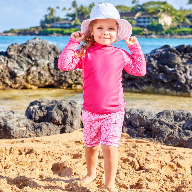 Little girl on the beach in UV Skinz's girl's long sleeve UPF swim shirt in hot pink mini medallion|hot-pink-mini-medallion