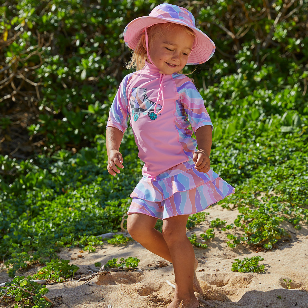 Little girl dancing on the beach in UV Skinz's swim hat in rollin along|oops-a-daisy